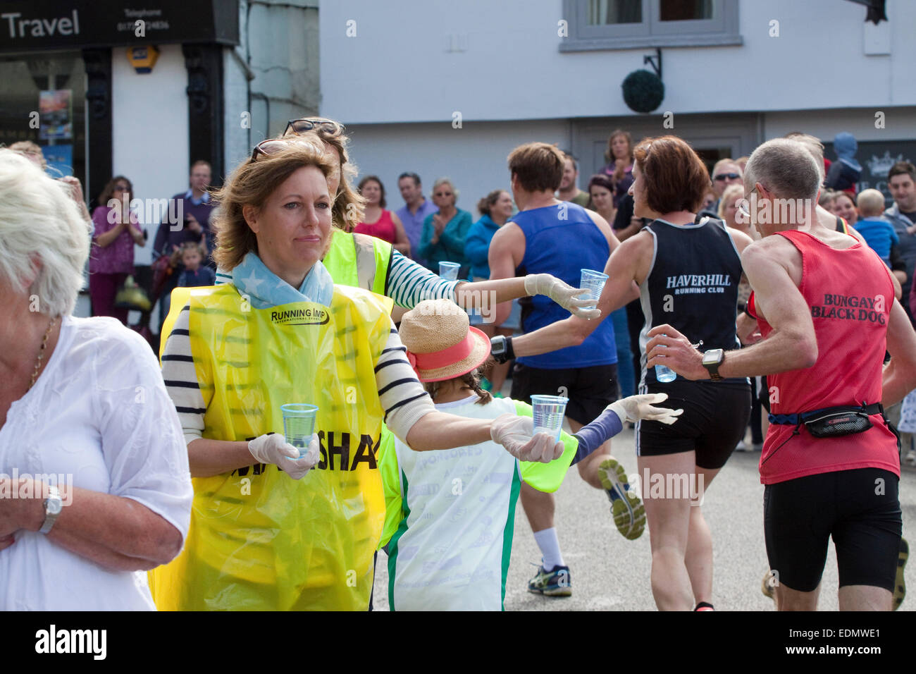 Les femmes et une adolescente dans un chapeau de paille d'exécuter un poste d'eau remise en place des gobelets en plastique d'eau aux coureurs dans une course sur route de 10k Banque D'Images