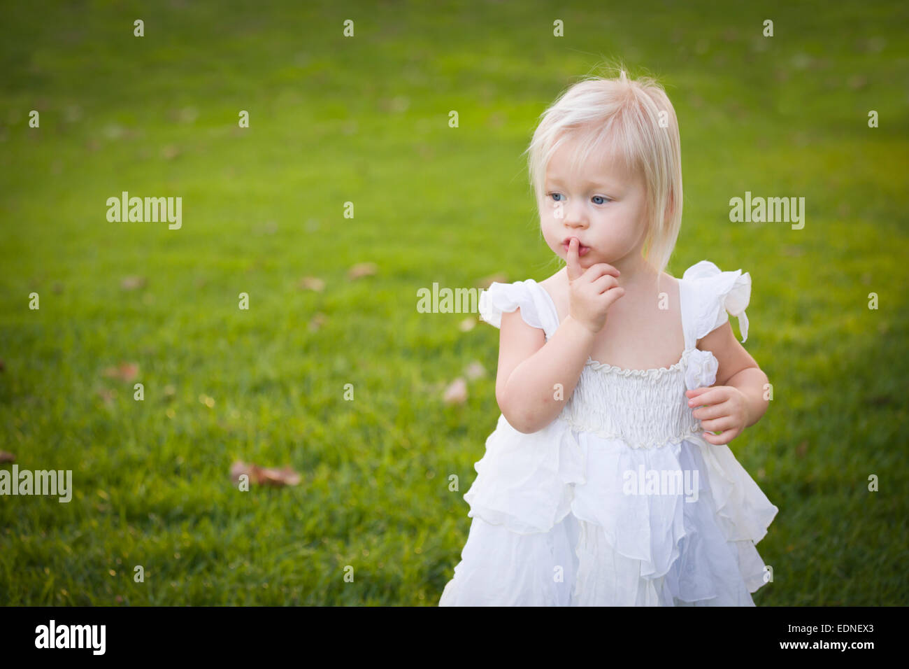 Belle adorable petite fille avec son doigt sur sa bouche le port de robe blanche dans un champ d'herbe. Banque D'Images