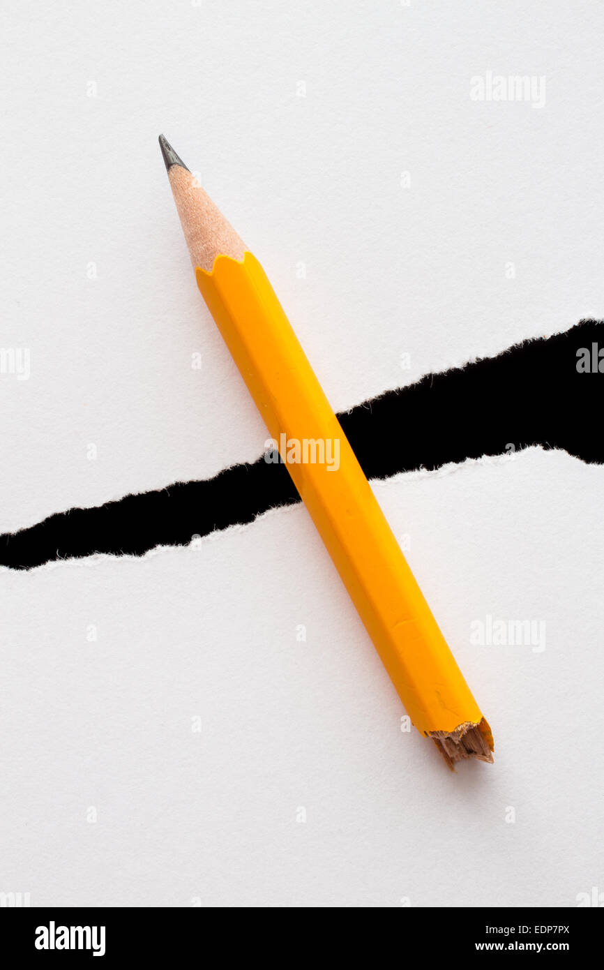 Crayon jaune brisée se trouve à travers un trou dans un morceau de papier blanc déchiré. Banque D'Images