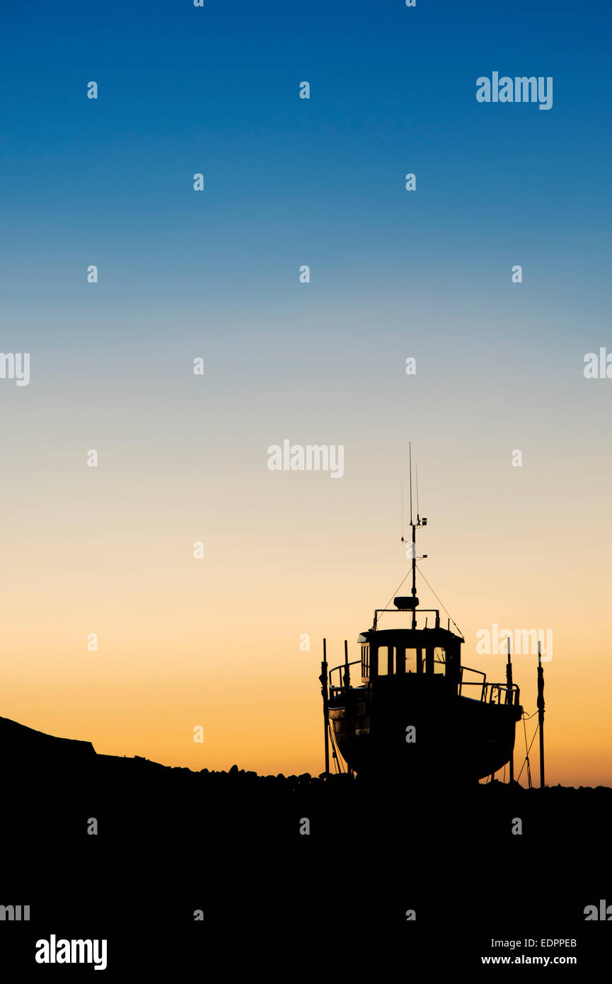 Bateau de pêche sur la terre ferme au lever du soleil dans le port de Lindisfarne, Holy Island, Northumberland, Angleterre. Silhouette Banque D'Images