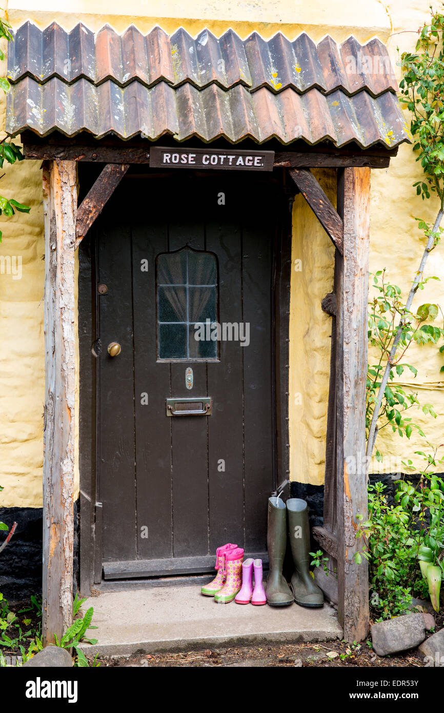 Bottes Wellington à l'avant porte de quaint cottage traditionnel en Bossington dans Exmoor, Somerset, Royaume-Uni Banque D'Images