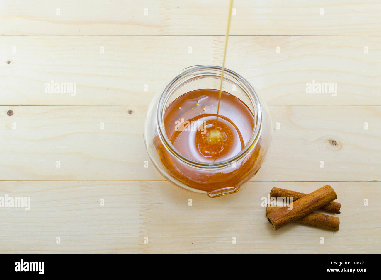 Des gouttes de miel dans un bocal en verre avec des bâtons de cannelle sur une table en bois Banque D'Images