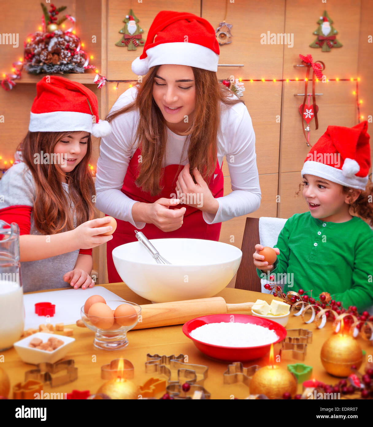 Mère heureuse avec deux enfants mignons porter du rouge Santa hat la cuisson festive alimentaire sur la cuisine, vacances de Noël concept Banque D'Images