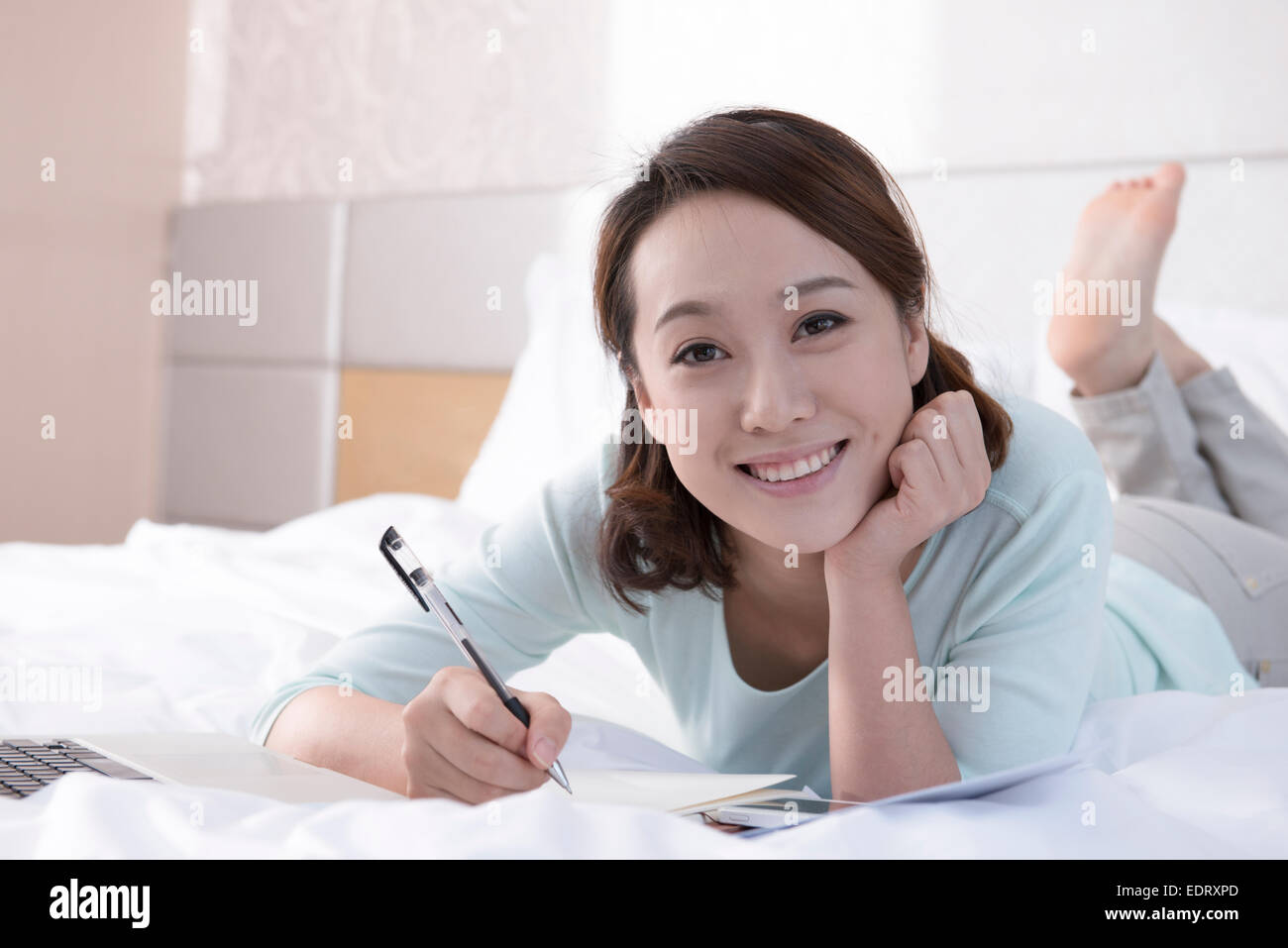 Jeune femme écrivant au lit Banque D'Images