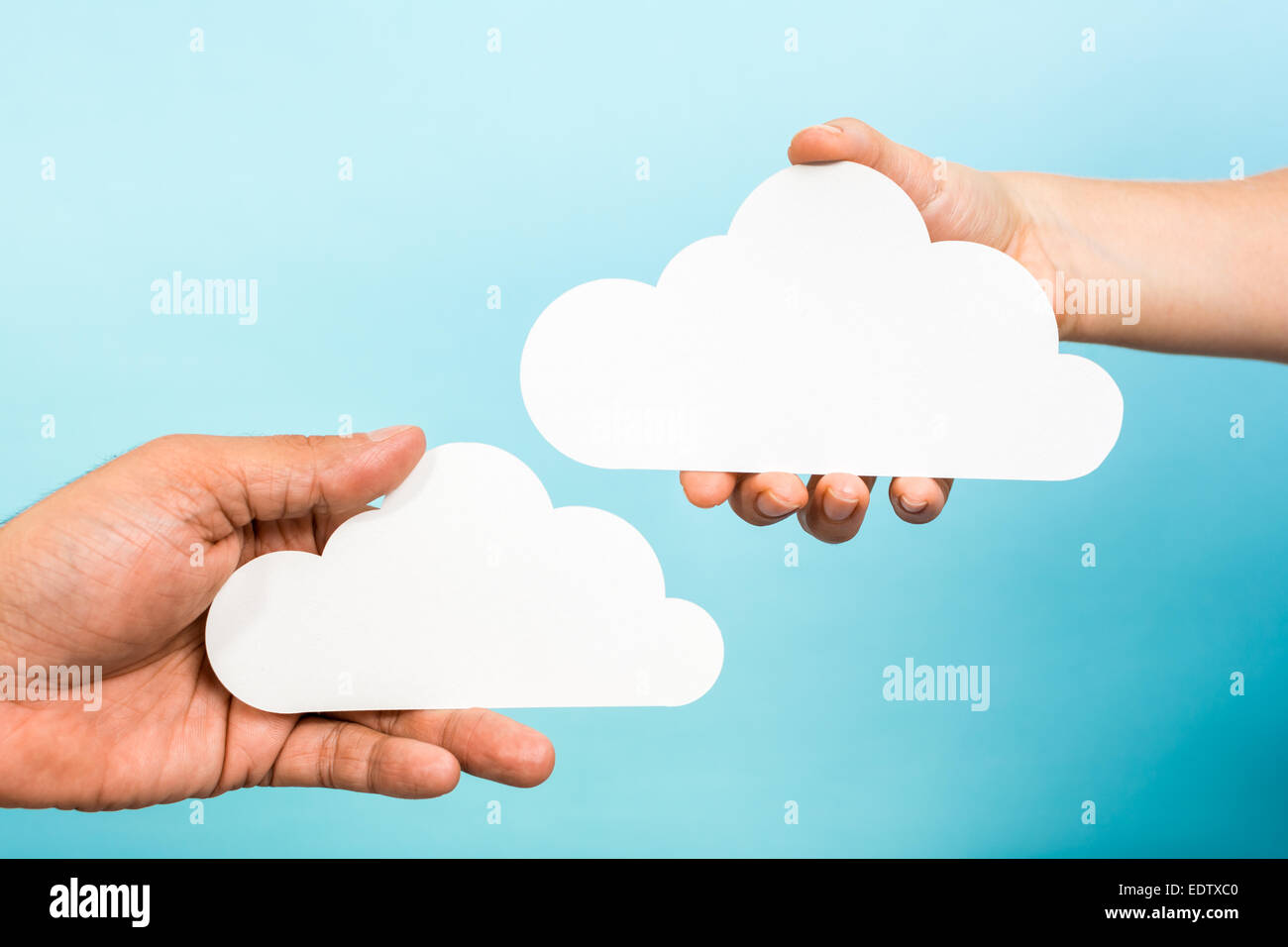 Deux mains tenant les nuages de papier sur fond bleu. Le concept de cloud computing. Banque D'Images