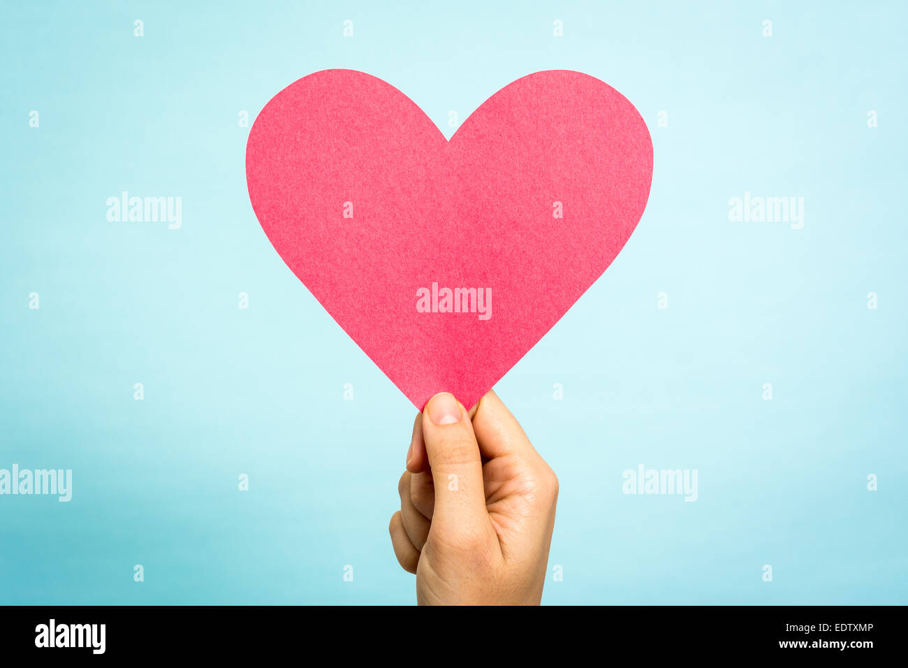 Main tenant papier rouge en forme de coeur d'amour sur fond bleu. Concept d'amour. Banque D'Images