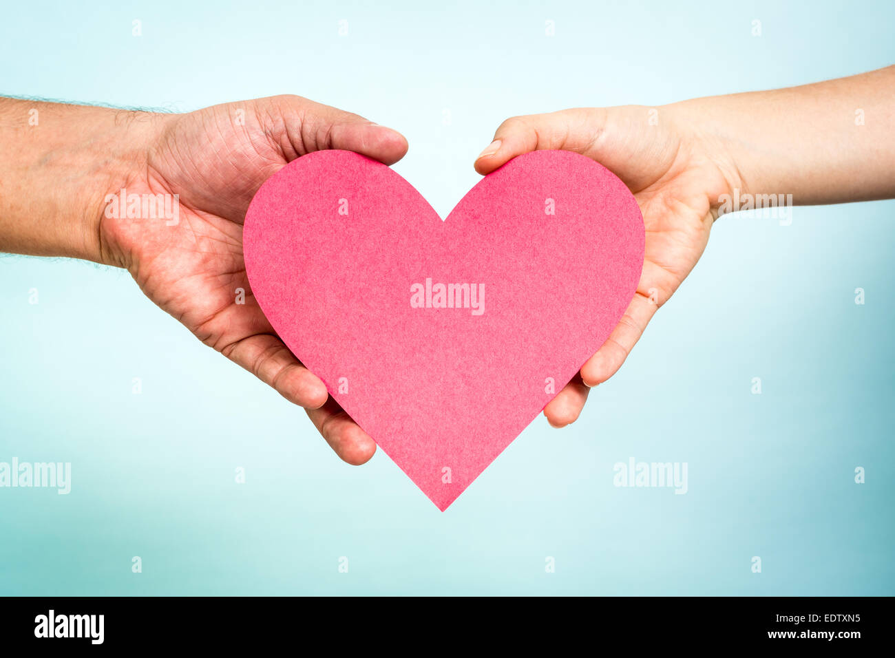 Deux mains tenant papier rouge en forme de coeur d'amour sur fond bleu. Concept d'amour. Banque D'Images
