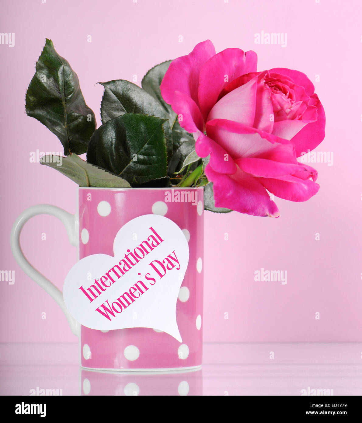 Heureux la Journée internationale des femmes accueil avec un rose rose et à pois sur fond rose tasse à café avec du texte. Banque D'Images