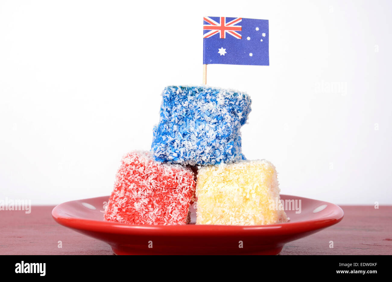 Heureux l'Australie jour rouge, blanc et bleu lamingtons cuisine de fête sur table en bois rouge contre l'arrière-plan blanc. Banque D'Images