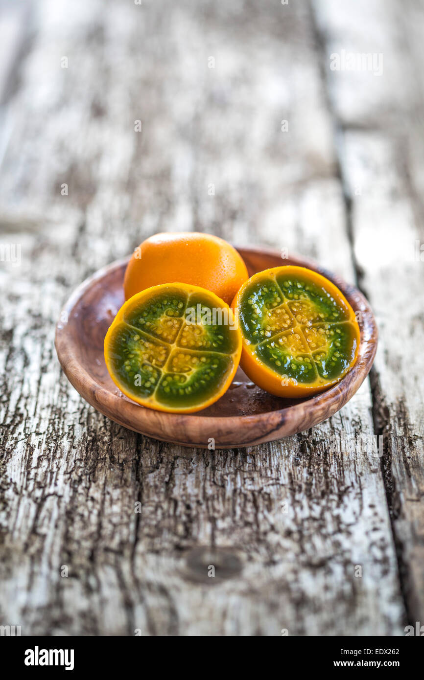 Couper vert vif et orange fleshed naranjilla dans un bol en bois sur table en bois rustique Banque D'Images