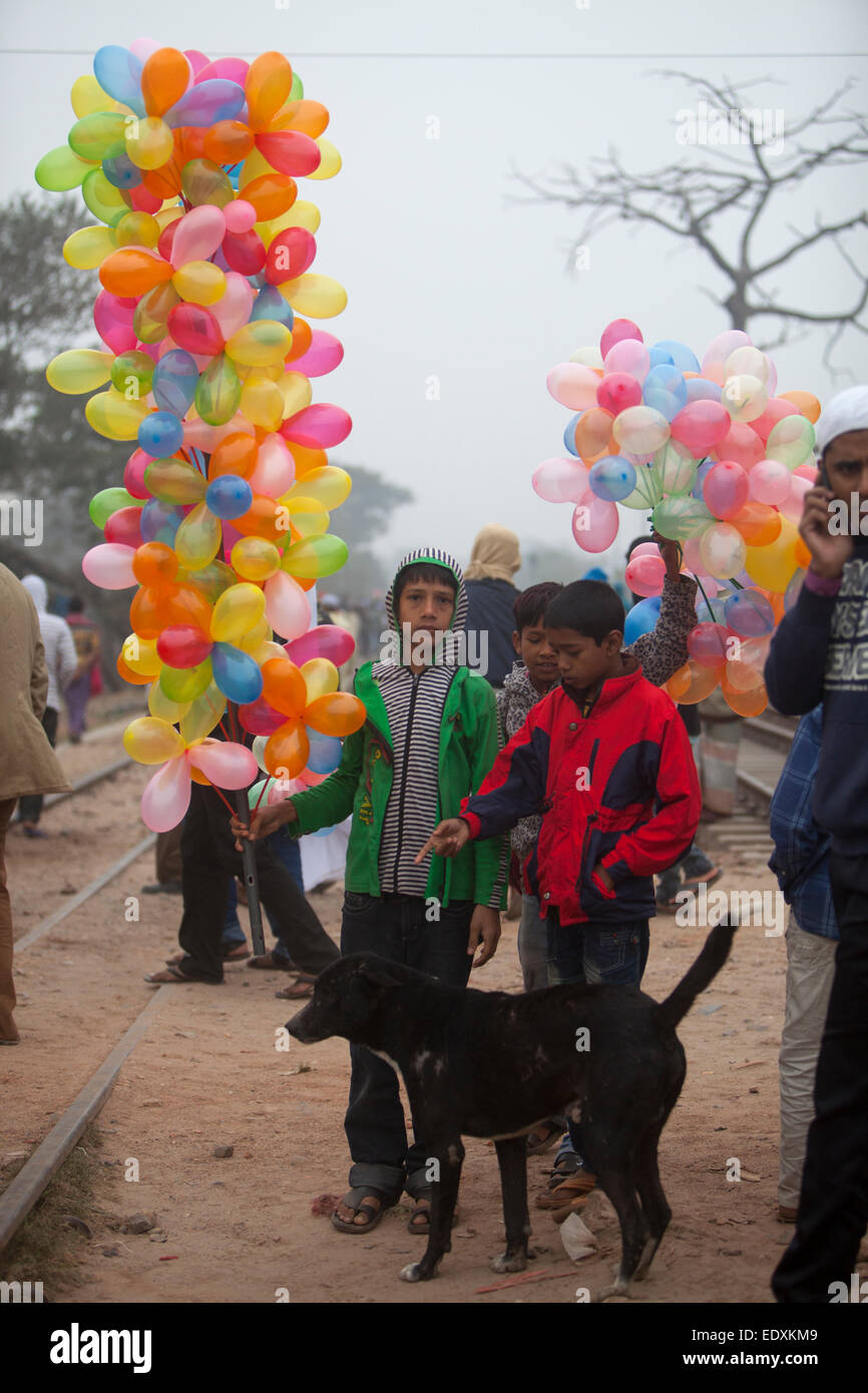 Garçon transporte bangladais des ballons pour vendre pendant qu'il observe les dévots musulmans à pied pour assister à la prière finale de la Congrégation islamique de trois jours sur les rives de la rivière Turag à Tongi, 20 kilomètres (13 milles) au nord de la capitale Dacca. Des centaines de milliers de Musulmans ont participé au congrès annuel de l'événement de trois jours qui est l'un des plus grands rassemblements religieux détenu depuis 1960 pour relancer les principes islamiques. Il dévalorise la politique et appelle à la paix. Banque D'Images