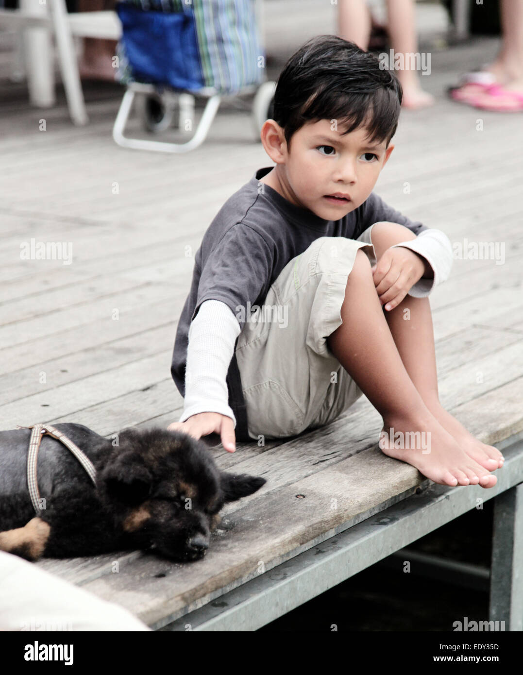 Cute little Asian Boy est caresser ou prendre soin d'un bébé chien allemand Shepard. Ils sont sur une plate-forme en bois à l'extérieur. Banque D'Images