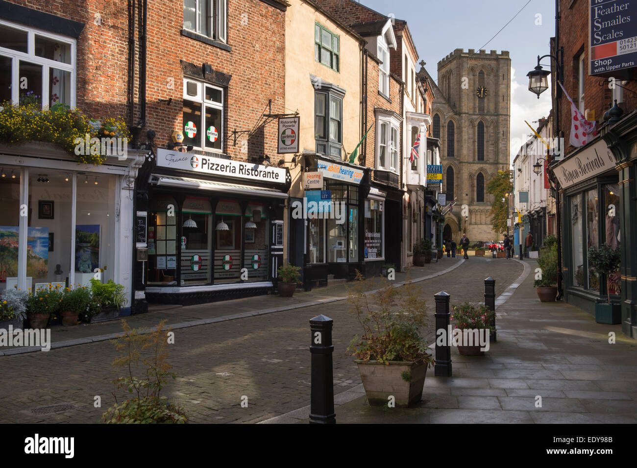 Regardant vers le bas, étroites, bordées de Kirkgate historique de petits magasins, vers une tour sur la façade ouest de la cathédrale de Ripon - North Yorkshire, Angleterre, Royaume-Uni. Banque D'Images