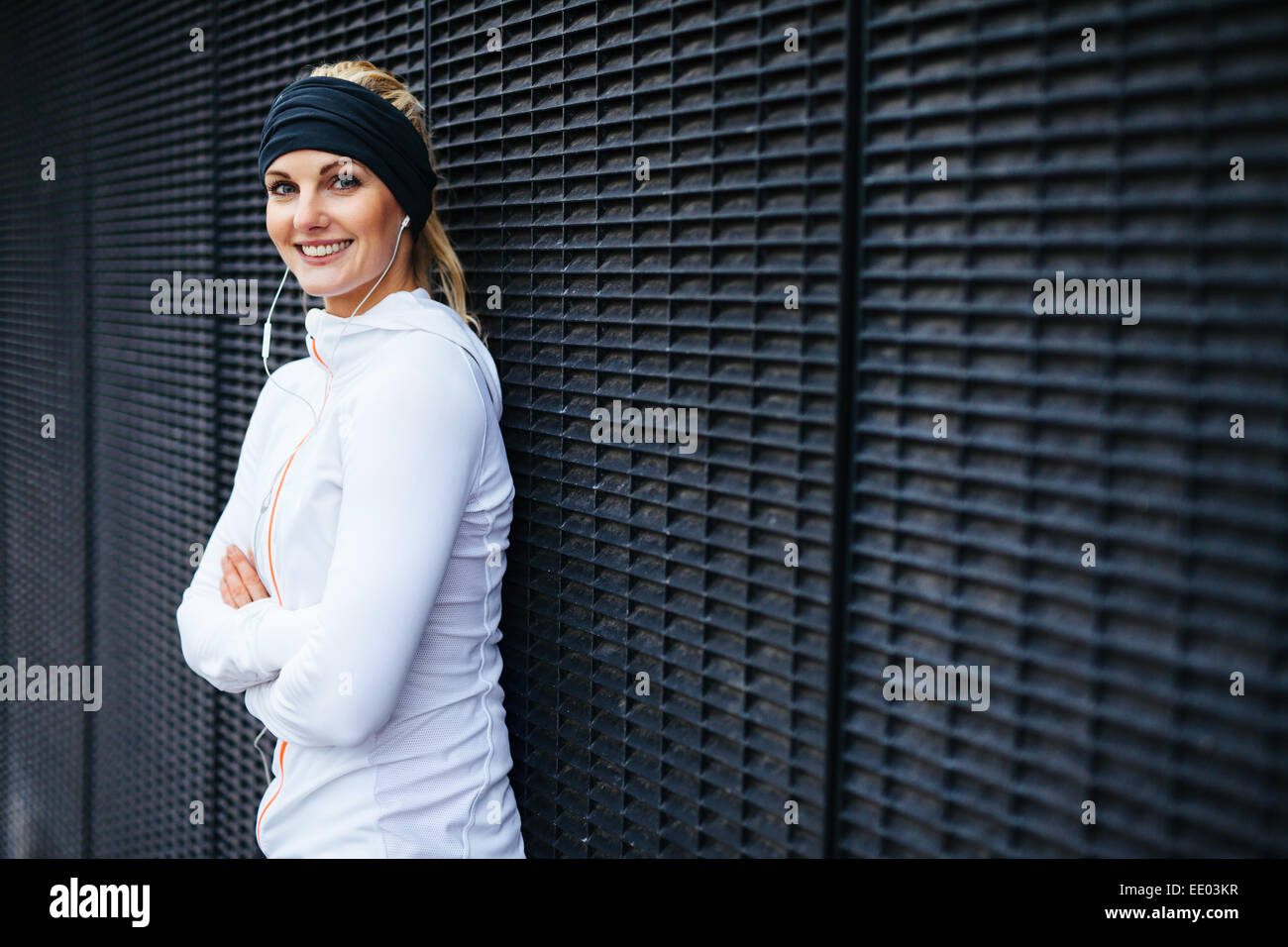 Portrait de la belle jeune femme en vêtements de sport à la caméra en souriant. Femme sportive appuyé contre un mur. Banque D'Images