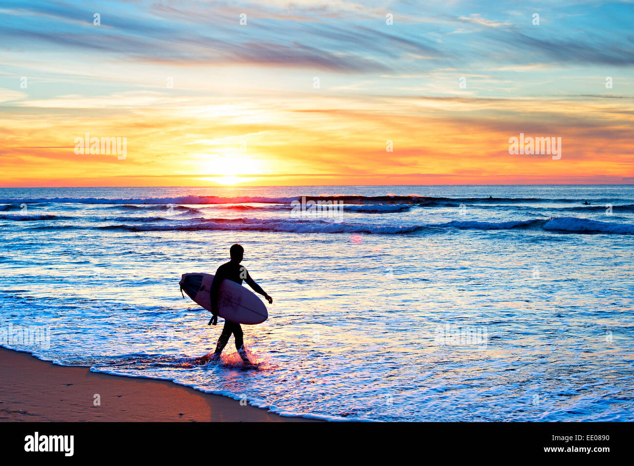 Surfer avec surf la marche sur la plage au coucher du soleil Banque D'Images