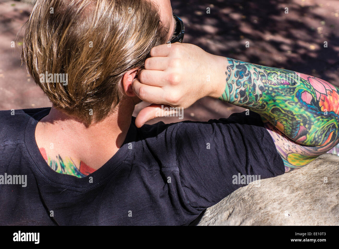Un homme avec un bras tatoué très coloré et une partie de son dos repose sur un banc avec une vue de derrière de ses tatouages à Ojai, CA Banque D'Images