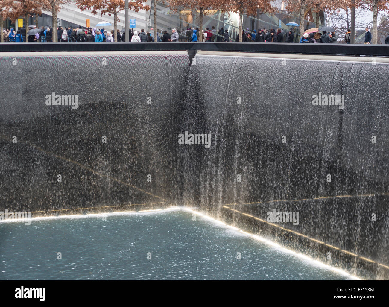 L'eau qui tombe au mémorial du 11 septembre à Ground Zero. Les touristes, bravant la pluie avec des parapluies, entourent la fosse profonde Banque D'Images