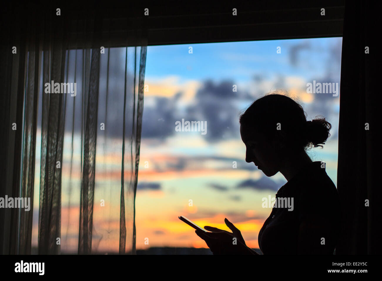 Une femme à l'aide de son comprimé à sa fenêtre d'hôtel alors que le soleil se couche sur Malmö, Suède. Banque D'Images