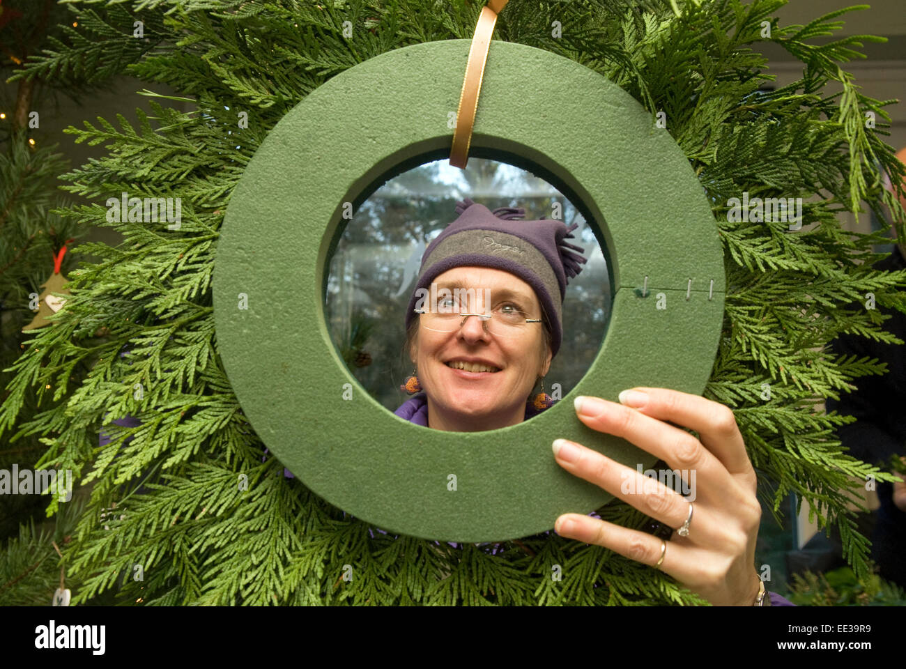 Femme dans un atelier de fabrication de couronnes de Noël admirer son terminé, création florale Witley, UK. Banque D'Images