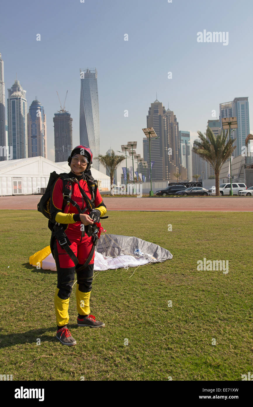 Le parachutisme girl atterri enregistrer sur l'herbe, en face de la sky scrapers de Dubaï. Elle sourit ainsi comme une dame oiseau. Banque D'Images