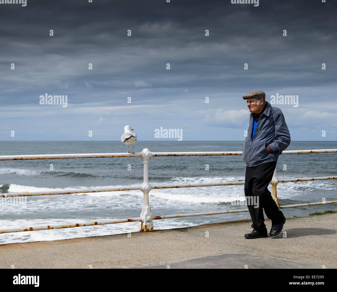 Un vieux homme marchant le long de la jetée de Whitby avec la mer du Nord à l'arrière-plan et un ciel nuageux. Banque D'Images