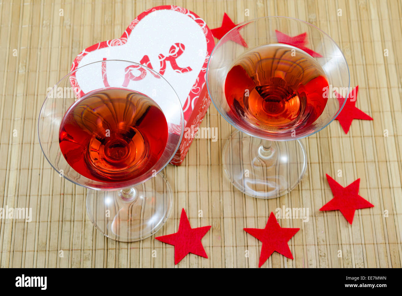 Deux verres d'une boisson alcoolique rouge en forme de cœur et des bougies sur une table de bambou Banque D'Images