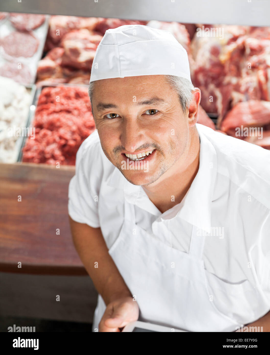 Portrait of happy butcher at display cabinet Banque D'Images