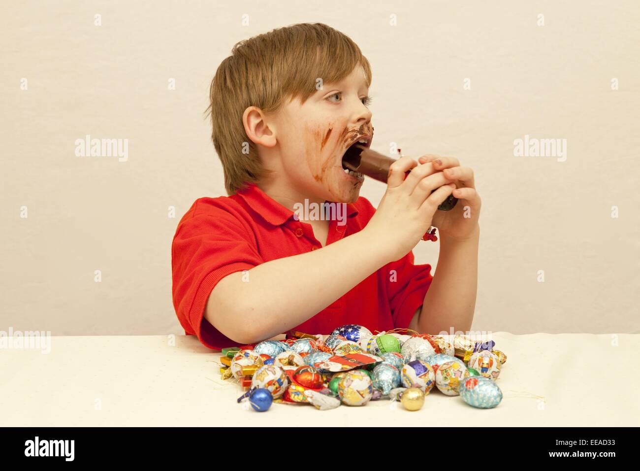 Jeune garçon avec un tas de friandises de Noël en face de lui manger un chocolat Santa Banque D'Images