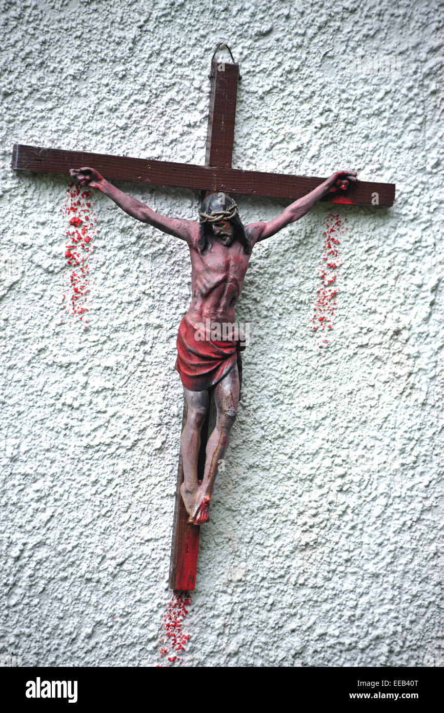 Le Christ sur une croix rouge sang couler de la peinture sur les mains et les pieds attachés à Pebble Dash wall Banque D'Images