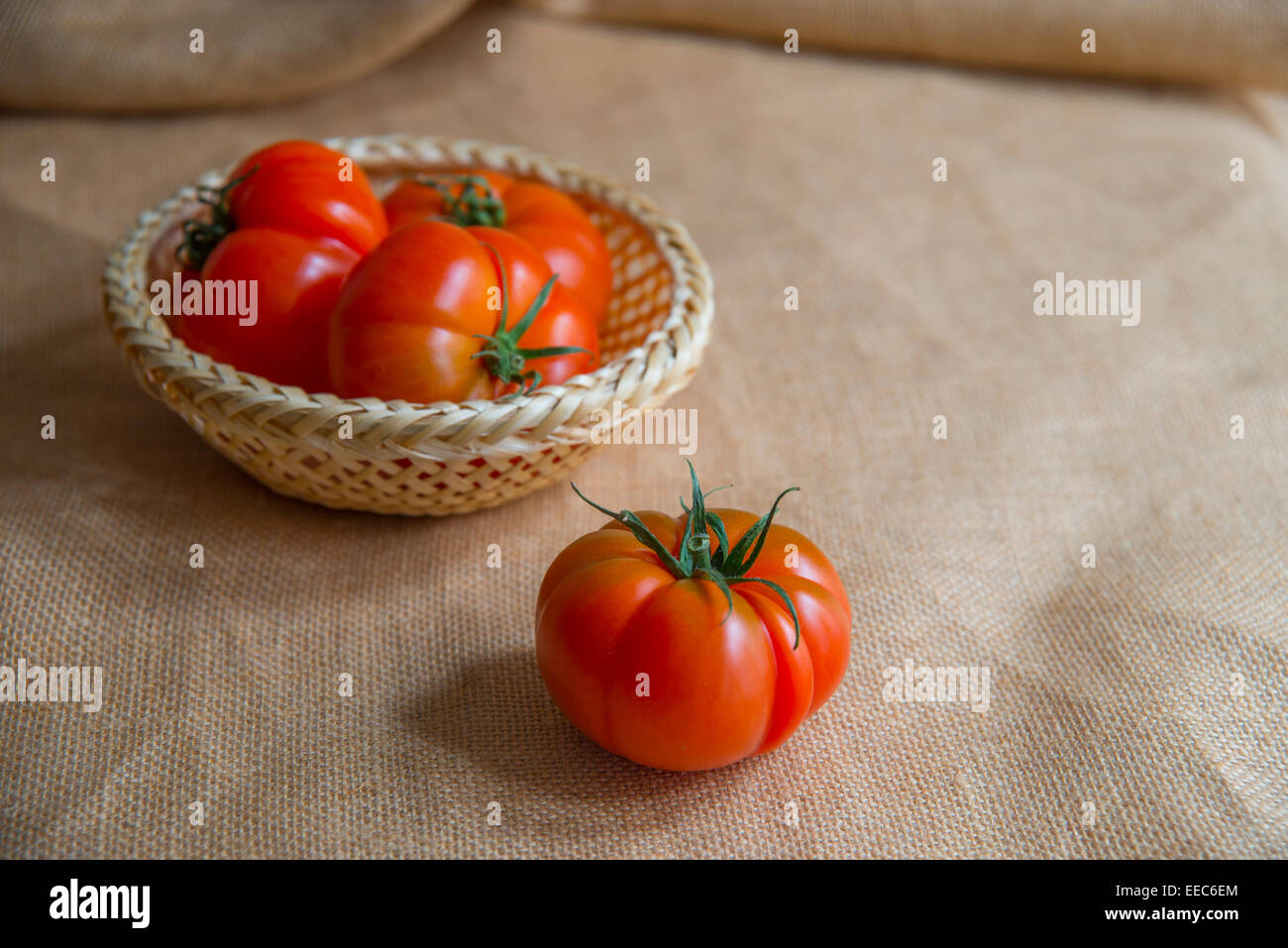 Quatre tomates, trois d'entre eux dans un panier. La vie encore. Banque D'Images