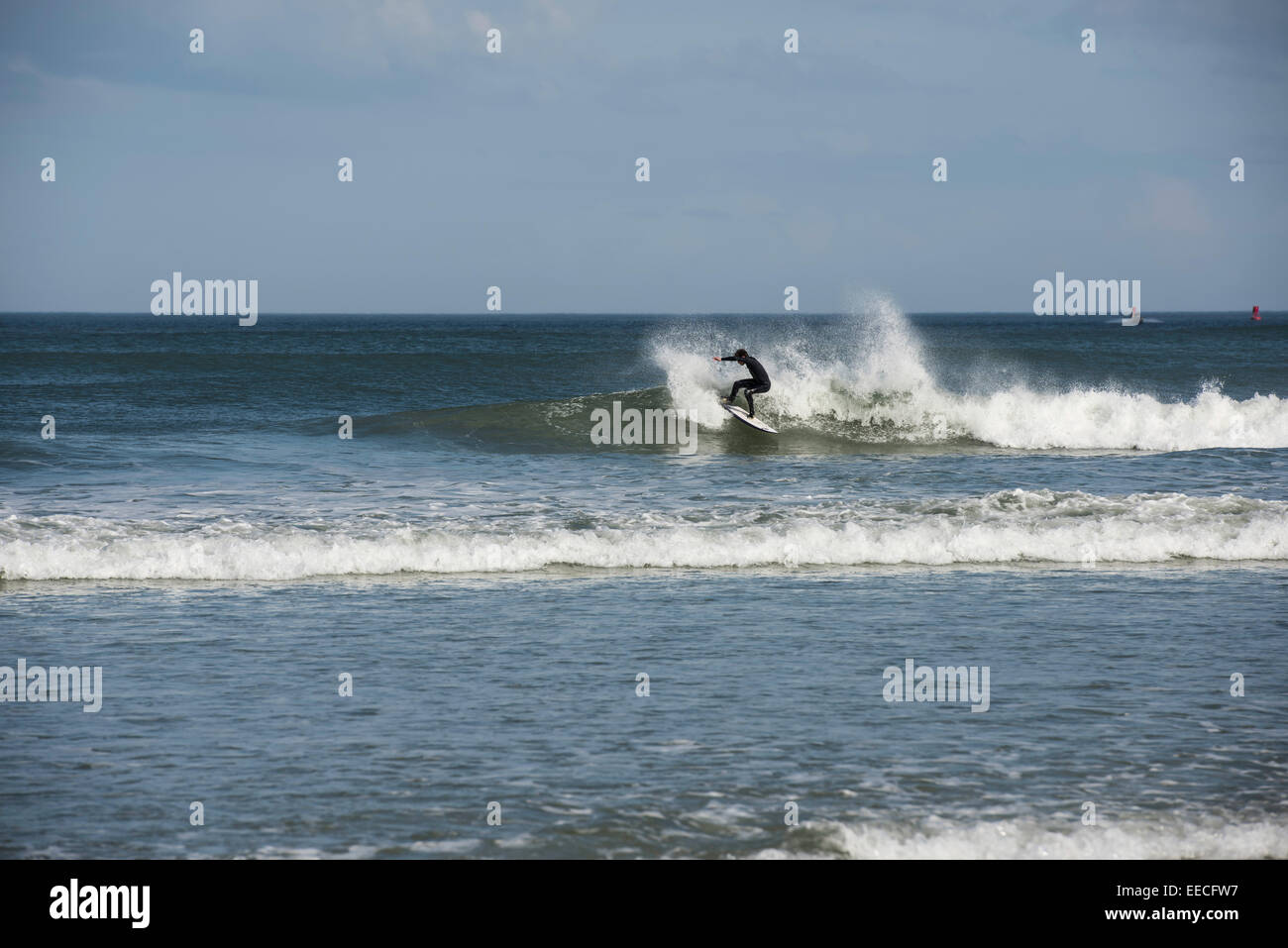 Une douzaine de mineurs combinaison noire réduit sur une vague qu'il surfe sur la côte est de la Floride près de Daytona Beach. Banque D'Images