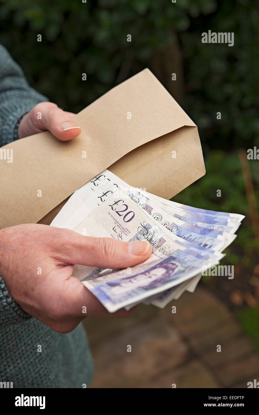 Gros plan de l'homme qui détient des billets en monnaie anglaise billets en espèces £20 billets de vingt livres et enveloppe marron Angleterre Royaume-Uni Grande-Bretagne Banque D'Images