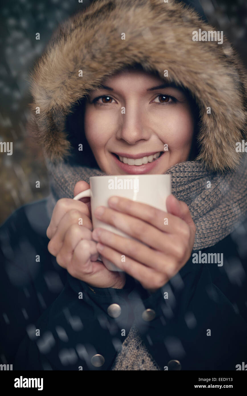 Jolie jeune femme en mode hiver chaud emmitouflé chaudement dans un épais manteau, écharpe en tricot et fur hat amplexicaule une tasse de thé chaud Banque D'Images
