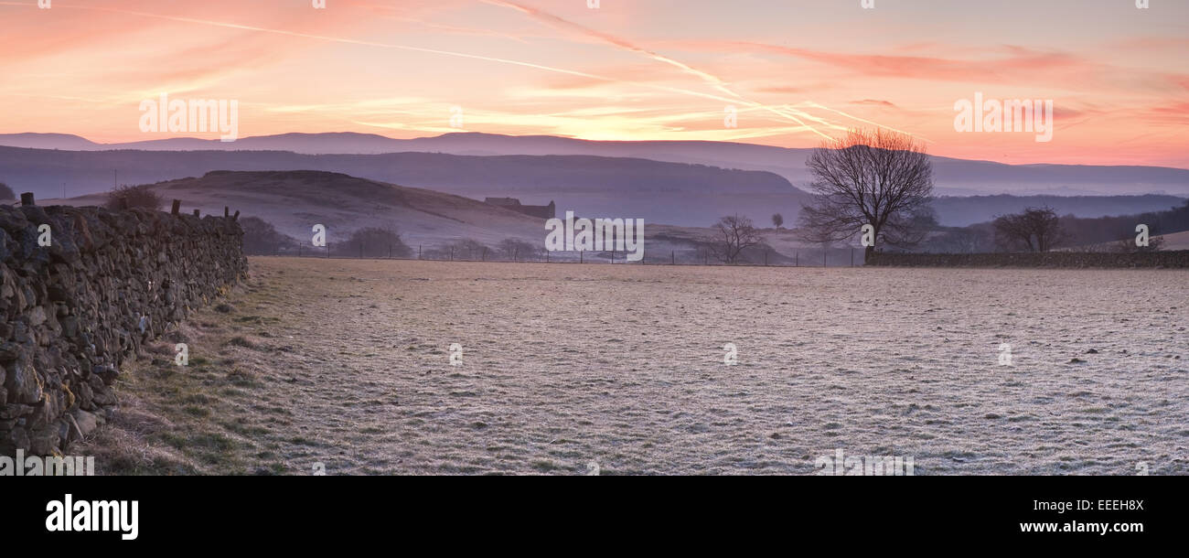 Champs couverts de givre et mur de pierres sèches sur les collines lointaines et les montagnes au lever du soleil Banque D'Images