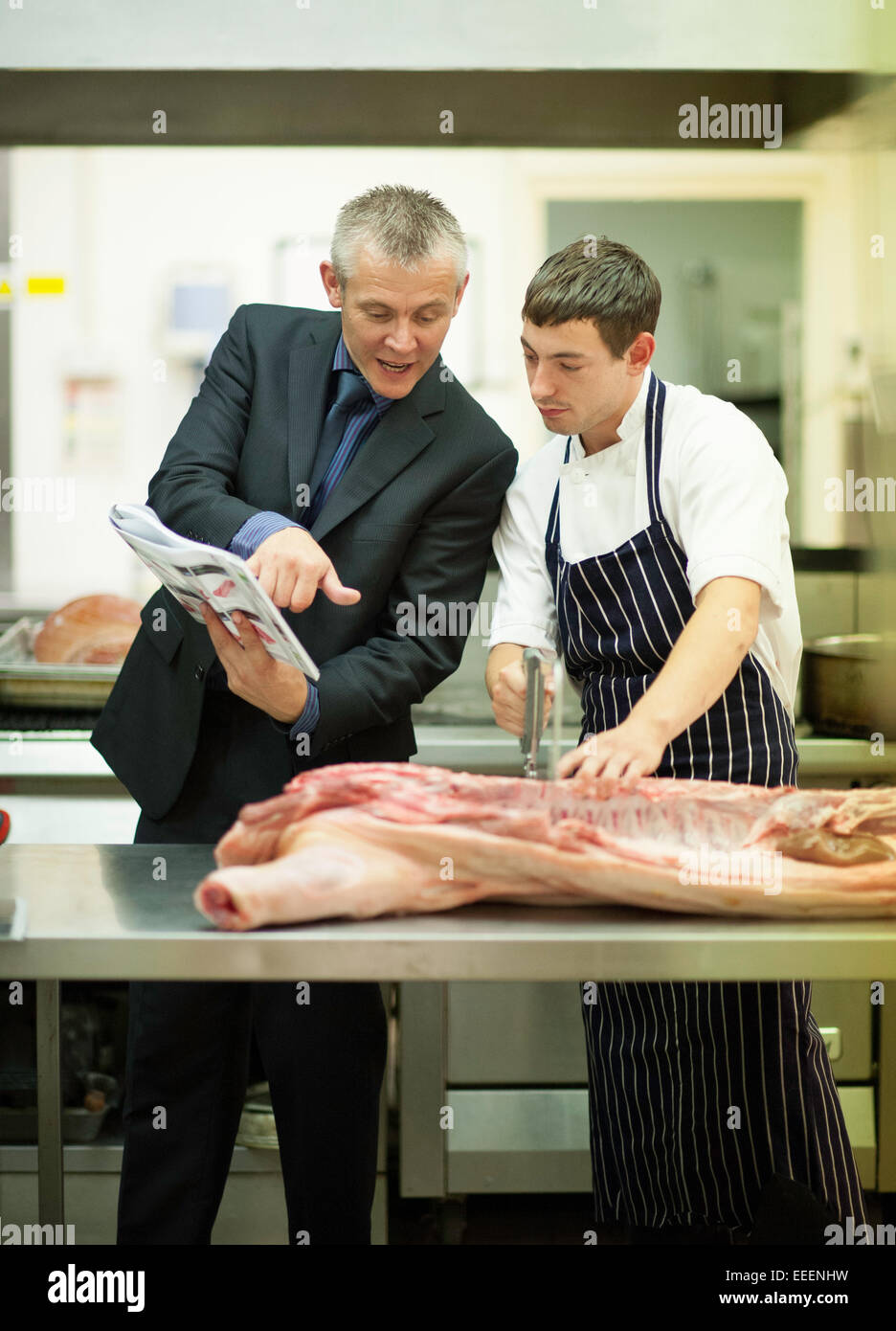 Un responsable l'enseignement d'un stagiaire boucher comment couper la viande Banque D'Images