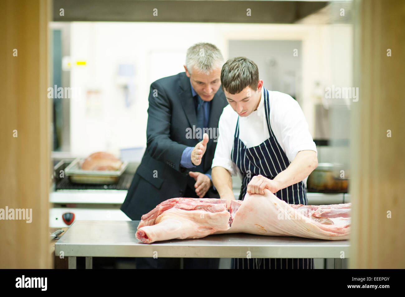 Un responsable l'enseignement d'un stagiaire boucher comment couper la viande Banque D'Images