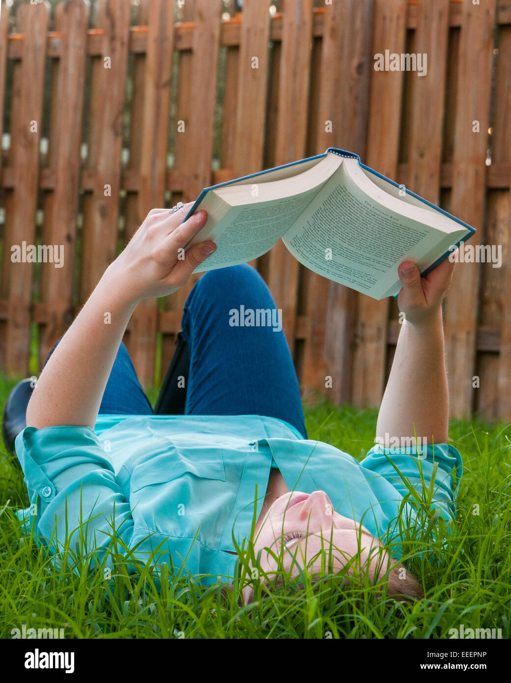 Femme couchée dans l'herbe haute de la lecture d'un livre Banque D'Images