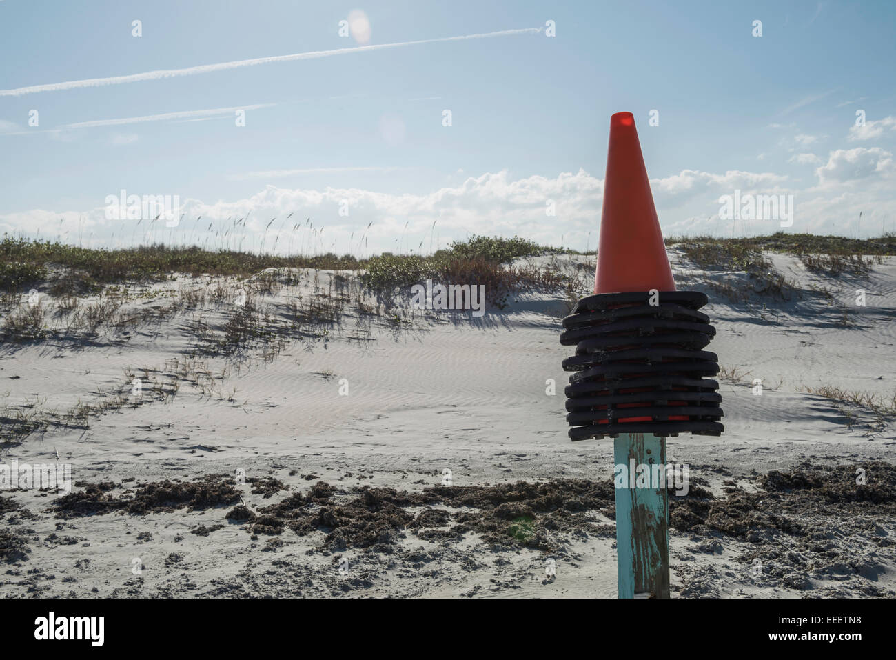 Des cônes de signalisation orange et noir empilés sont placés au sommet d'un poteau en bois avec une peinture bleu clair et abîmé devant les dunes de sable de Daytona Beach, en Floride. Banque D'Images