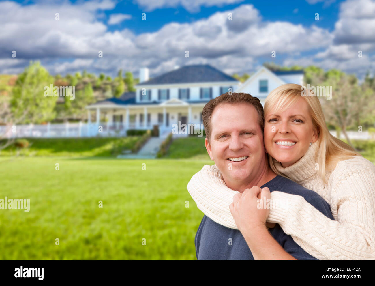 Happy Young Couple Sitting in front of a Beautiful House. Banque D'Images