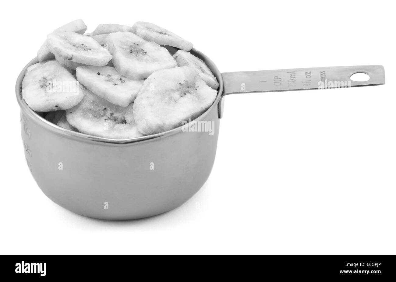 Chips de banane séchée dans un tasse mesure, isolé sur fond blanc - traitement monochrome Banque D'Images