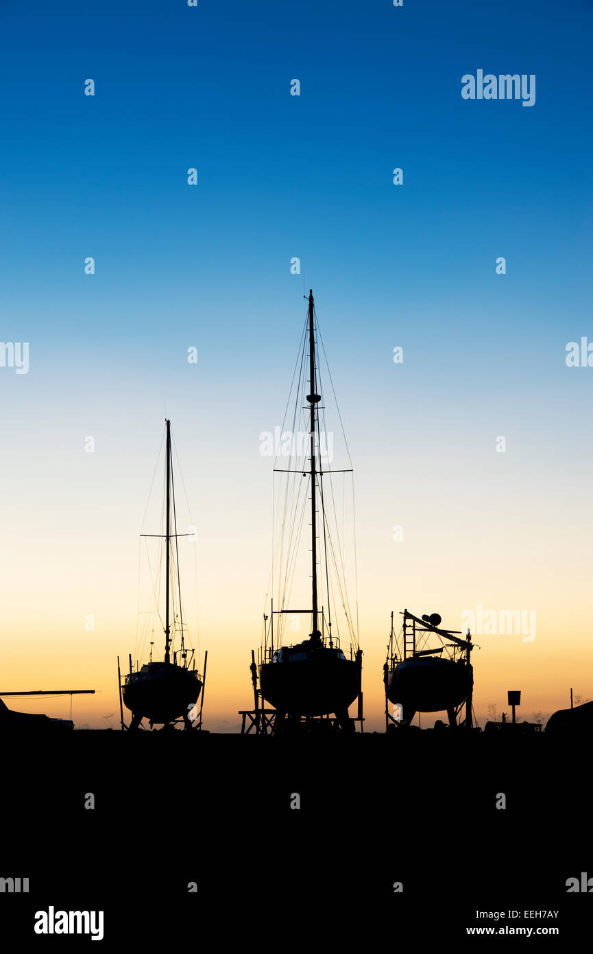 Bateaux à voile sur la terre ferme au lever du soleil dans le port de Lindisfarne, Holy Island, Northumberland, Angleterre. Silhouette Banque D'Images