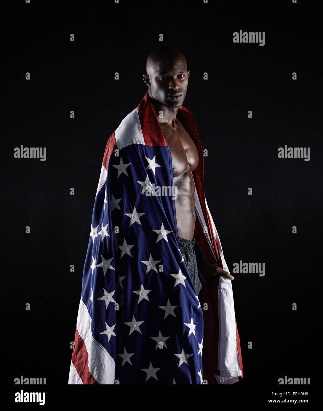 Portrait de l'athlète Afro enveloppé dans USA flag sur fond noir. Carrossier avec le drapeau américain en studio. Banque D'Images