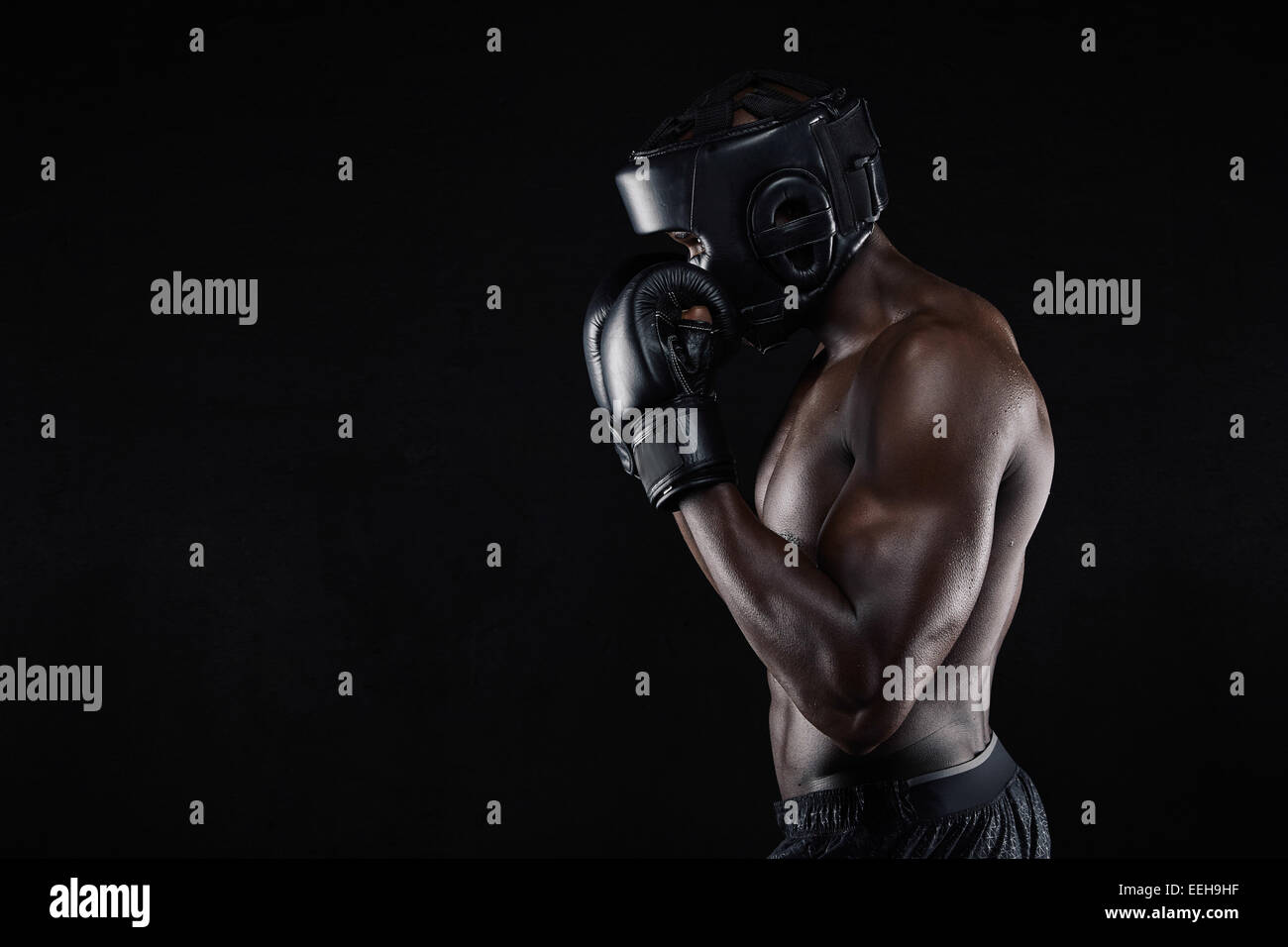Vue latérale d'un jeune male boxer dans une position de combat sur fond noir. African Male boxer bloquant son visage avec des gants. Banque D'Images