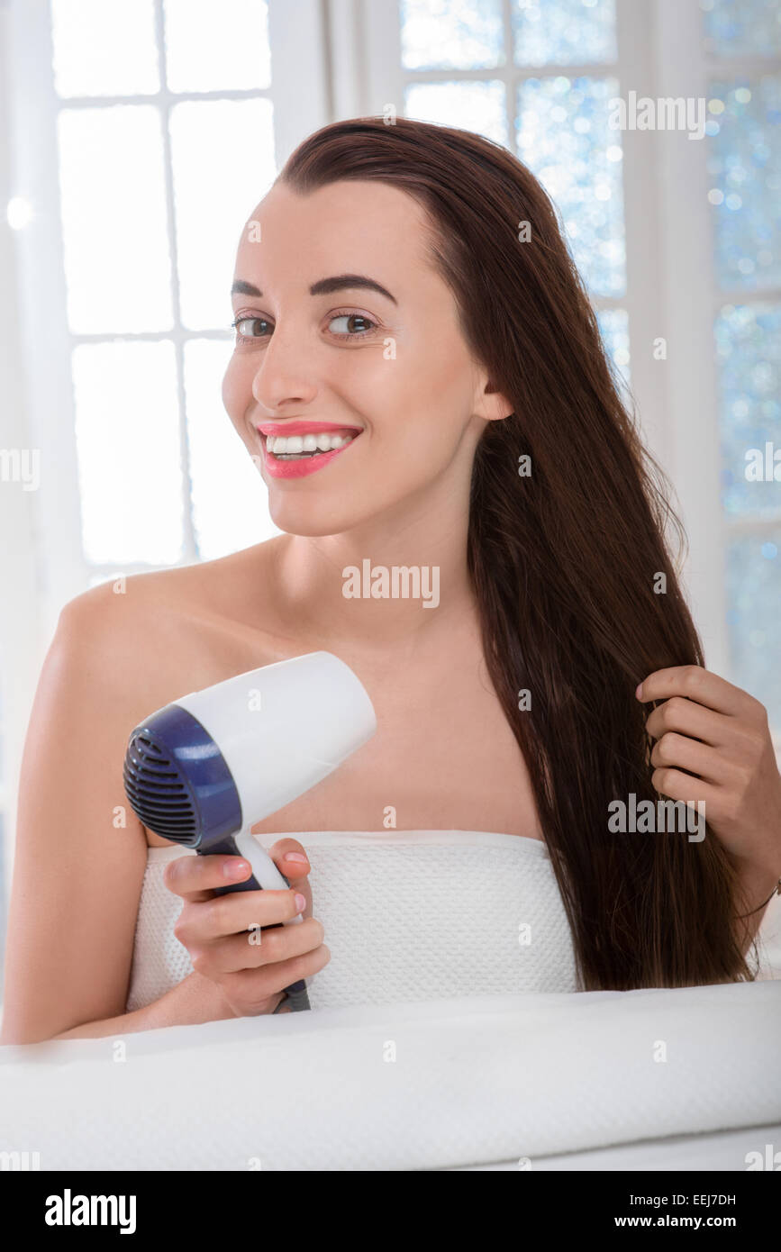 Jeune femme aux longs cheveux noirs et des cheveux de séchage avec un sèche-cheveux dans la salle de bains Banque D'Images