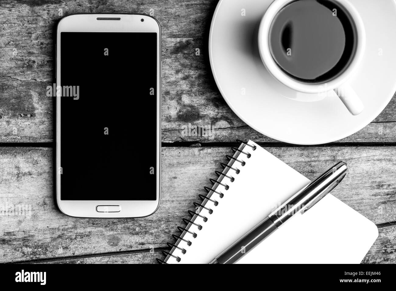 Pause café top view image en noir et blanc. Smartphone avec bloc-notes, stylo et tasse de café. Banque D'Images