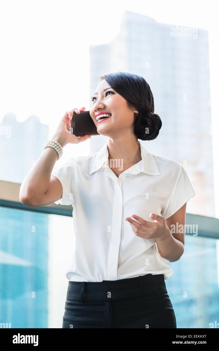 Femme d'affaires chinois à l'aide de téléphone sur terrasse en face de city skyline Banque D'Images