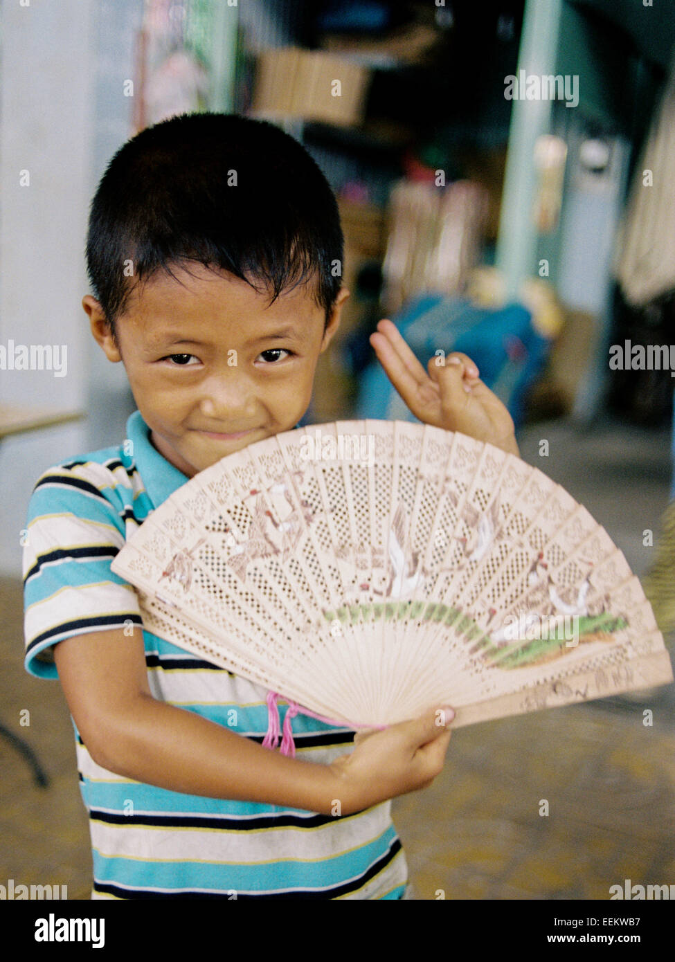 Portrait of happy Young boy holding vietnamiens ventilateur pliant smiling in village sur le delta du Mékong Banque D'Images