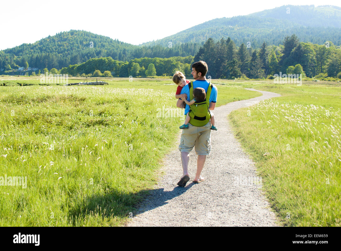 Père marchant le long d'un sentier transportant son fils et sa fille