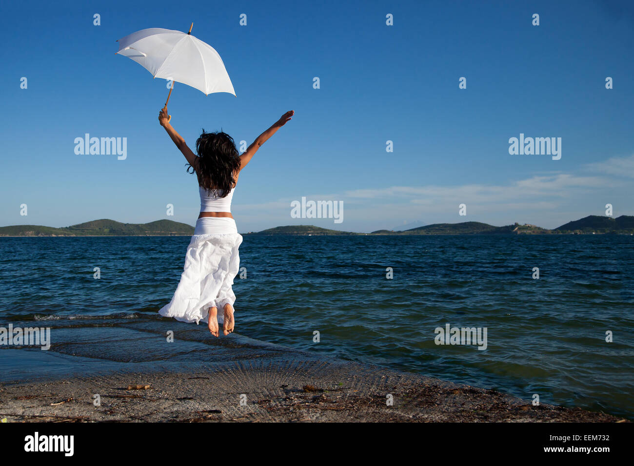 Jeune femme en blanc holding umbrella jumping on beach Banque D'Images