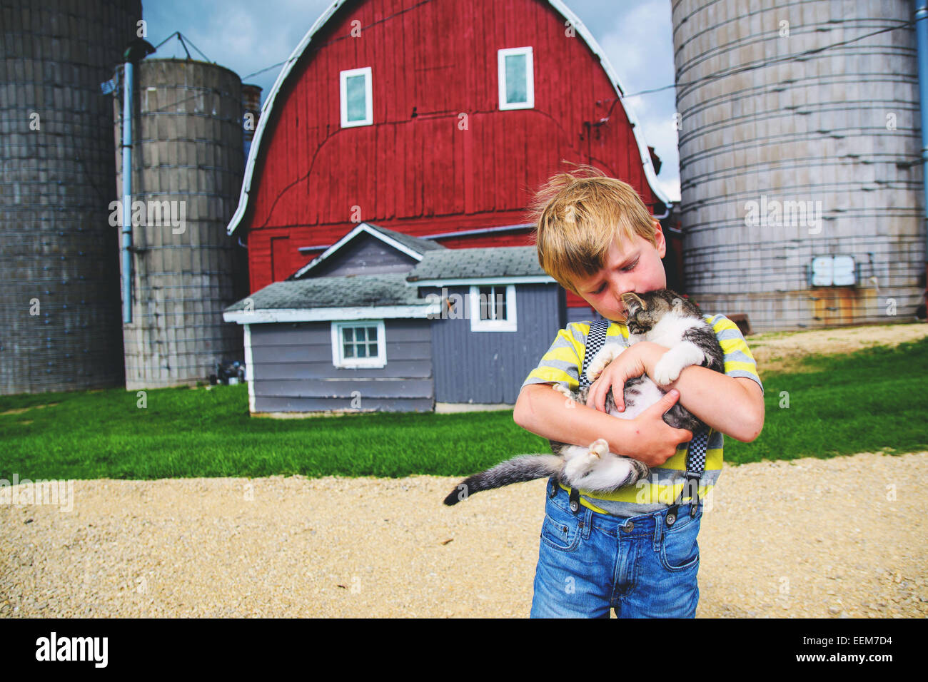 Boy (3-4) holding cat in front of farm barn Banque D'Images